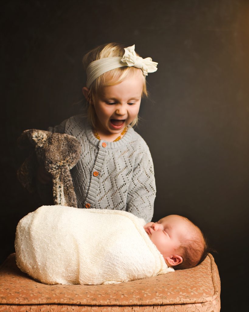 Big sister looking at newborn baby. Everything You Need to Know About Newborn Photography
