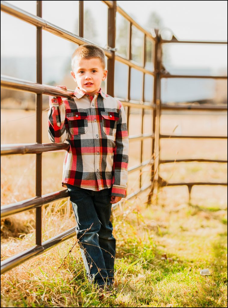 Boy standing along horse fence wearing plaid