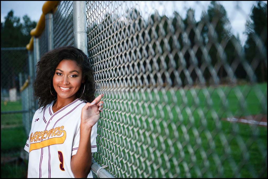 Ellensburg Senior Portraits of girl in softball uniform against fence