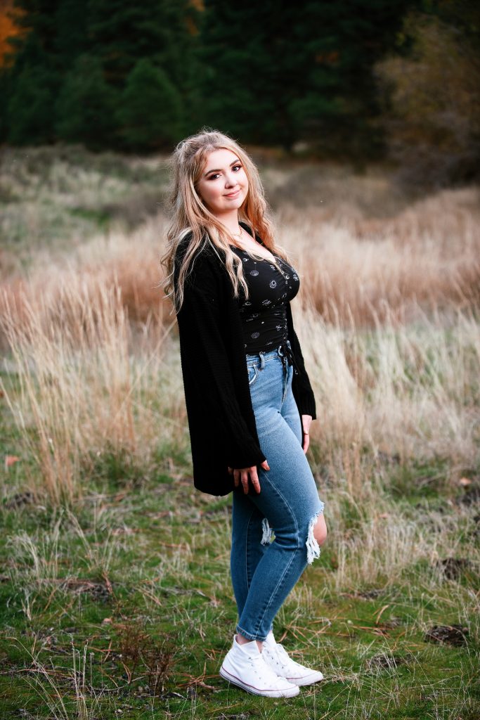 Girl posing for her senior pictures wearing a black sweater and blue jeans