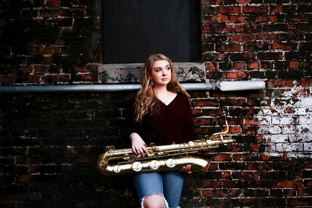 Pretty girl posing with a saxophone in an urban setting for senior pictures