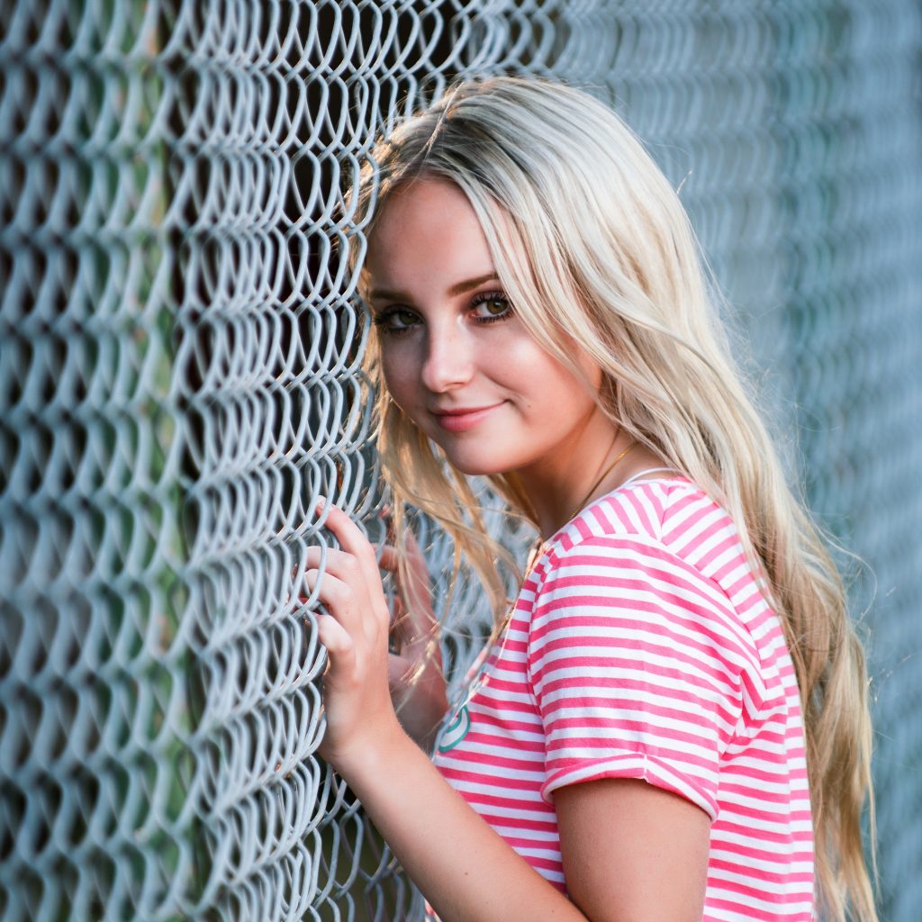 Senior Photography in Ellensburg blonde high school girl poses against chain link fence