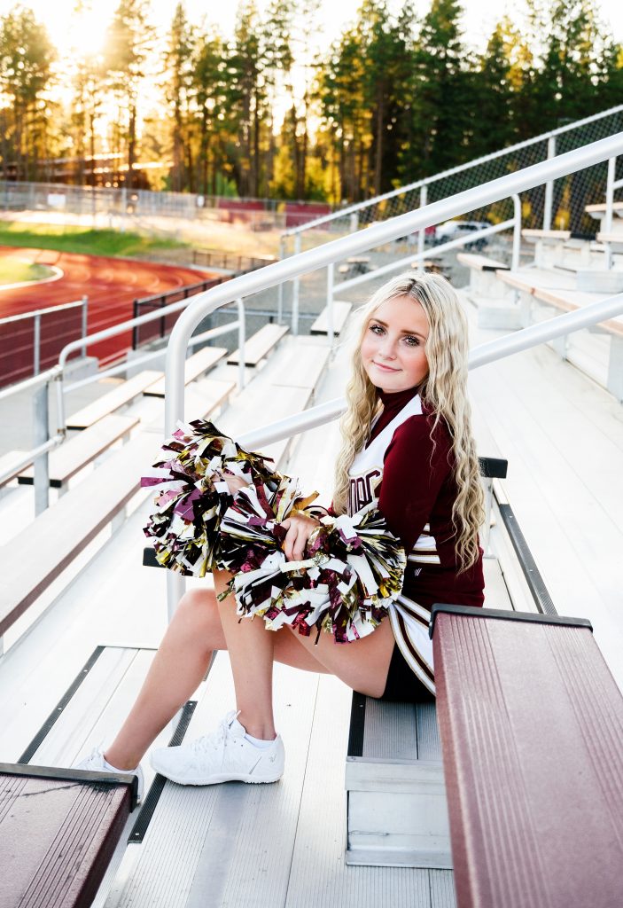 Senior Photography in Ellensburg a blonde cheer leader posing on bleachers with her pom poms