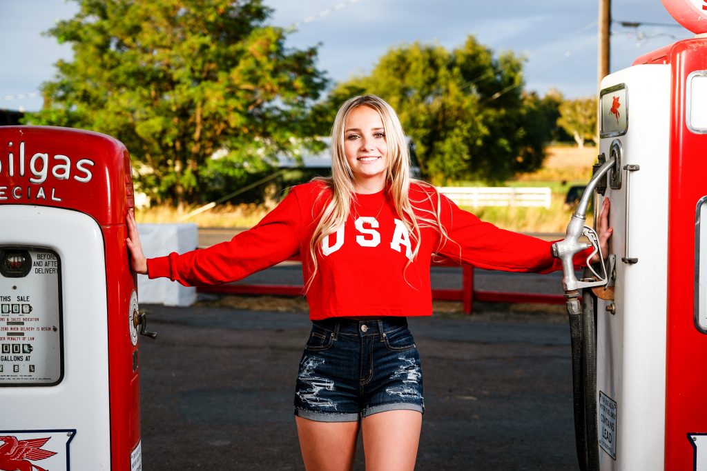 Senior Photography in Ellensburg, a young blonde girl with long hair posing with vintage gas pump