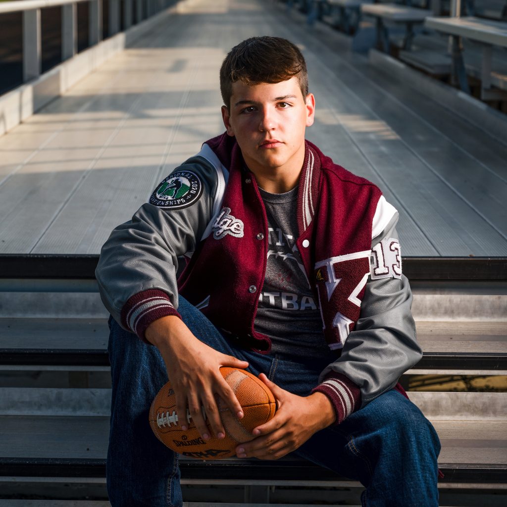 highschool senior photographer high school athlete in letterman jacket holding football
