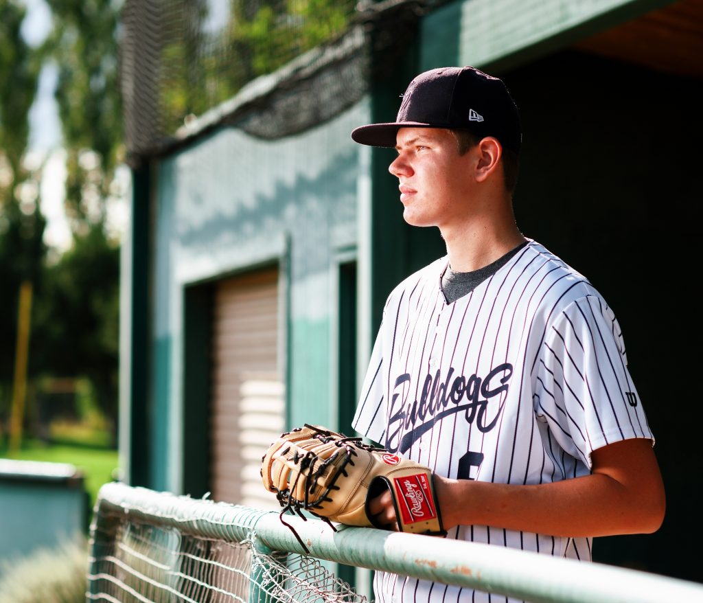 Senior Photos in Ellensburg baseball player leans against fence wearing baseball mit on hand