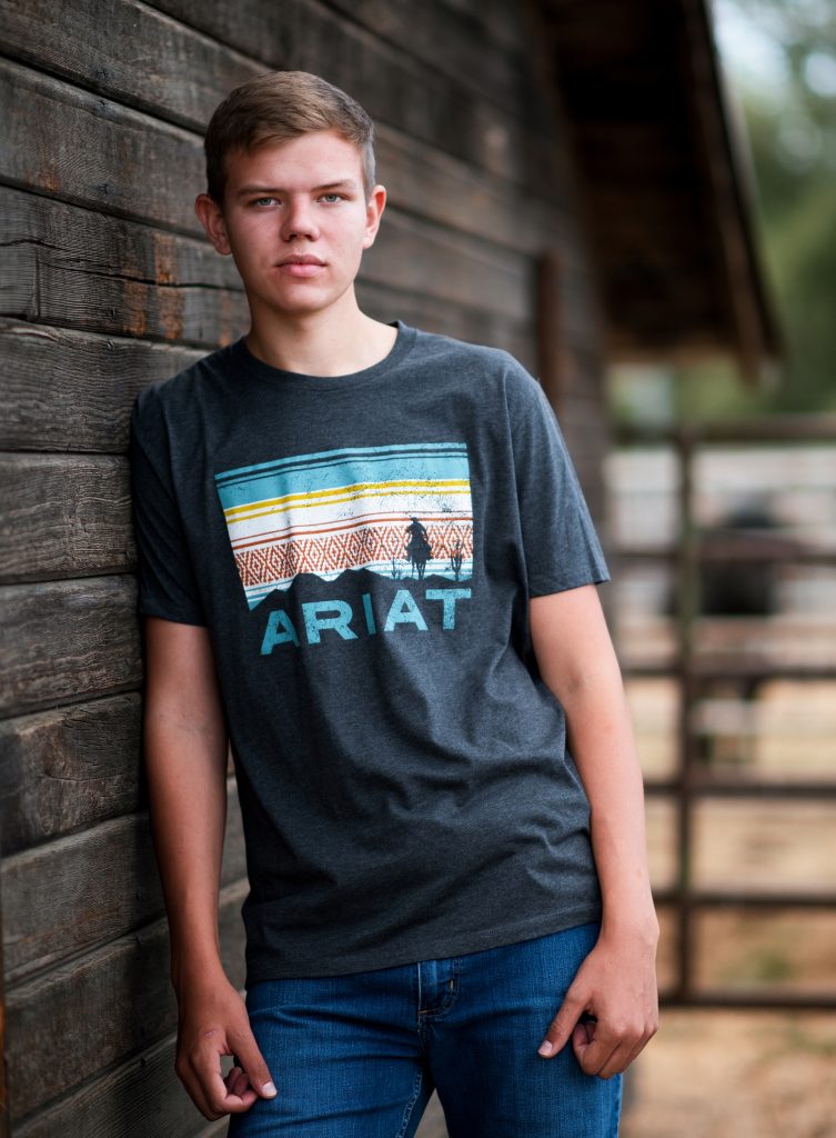 Senior Photos in Ellensburg student in ariat shirt leans casually against wooden barn