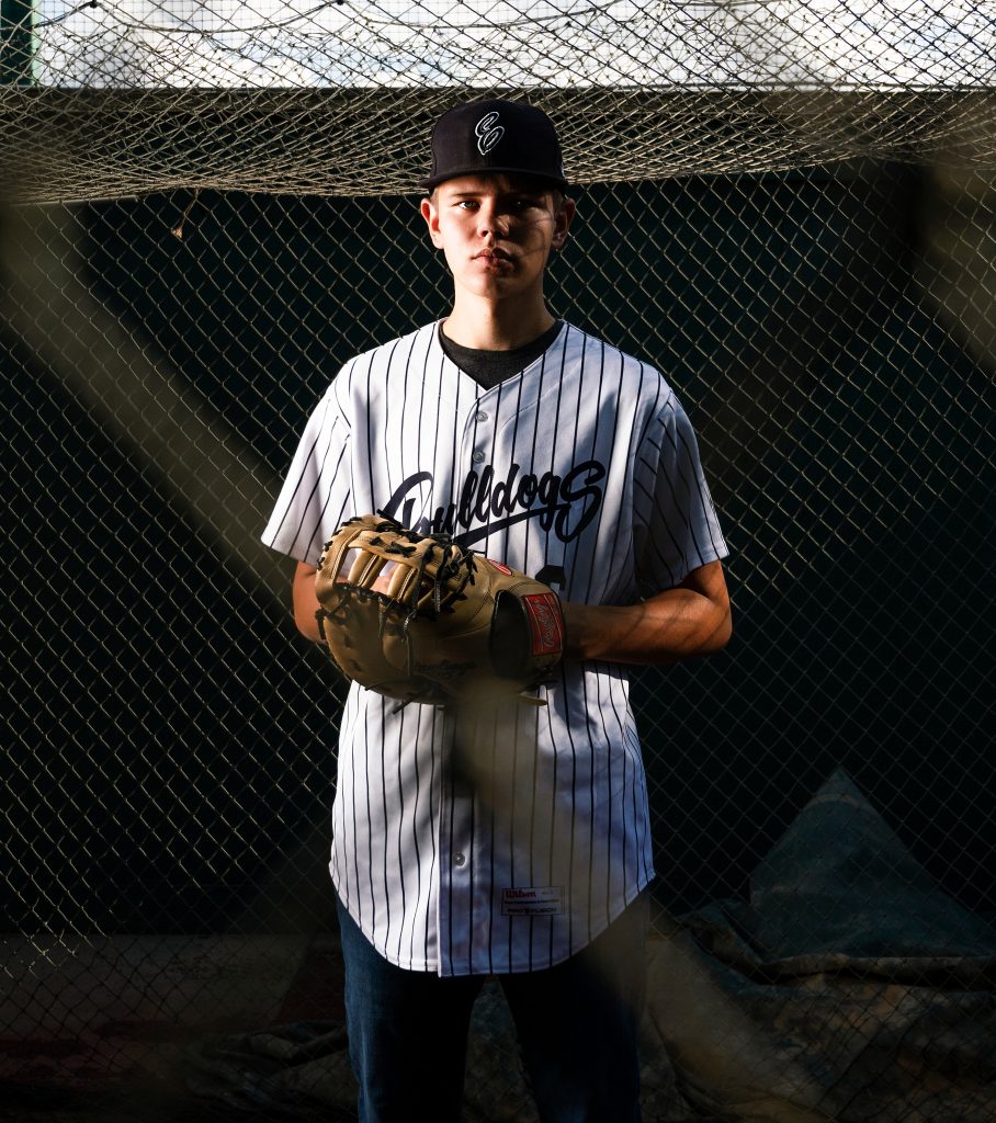 Senior Photos in Ellensburg baseball player stands infront of the net wearing a mit and serious expression