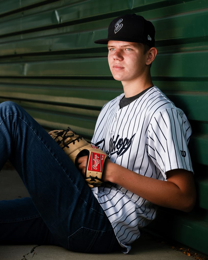 Senior Photos in Ellensburg baseball player leans against the dugout wearing a baseball mit