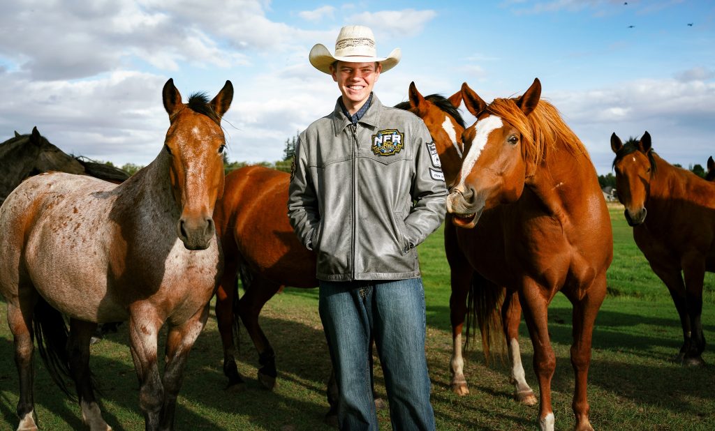 Senior Photos in Ellensburg boy stands in the pasture with horses surrounding him