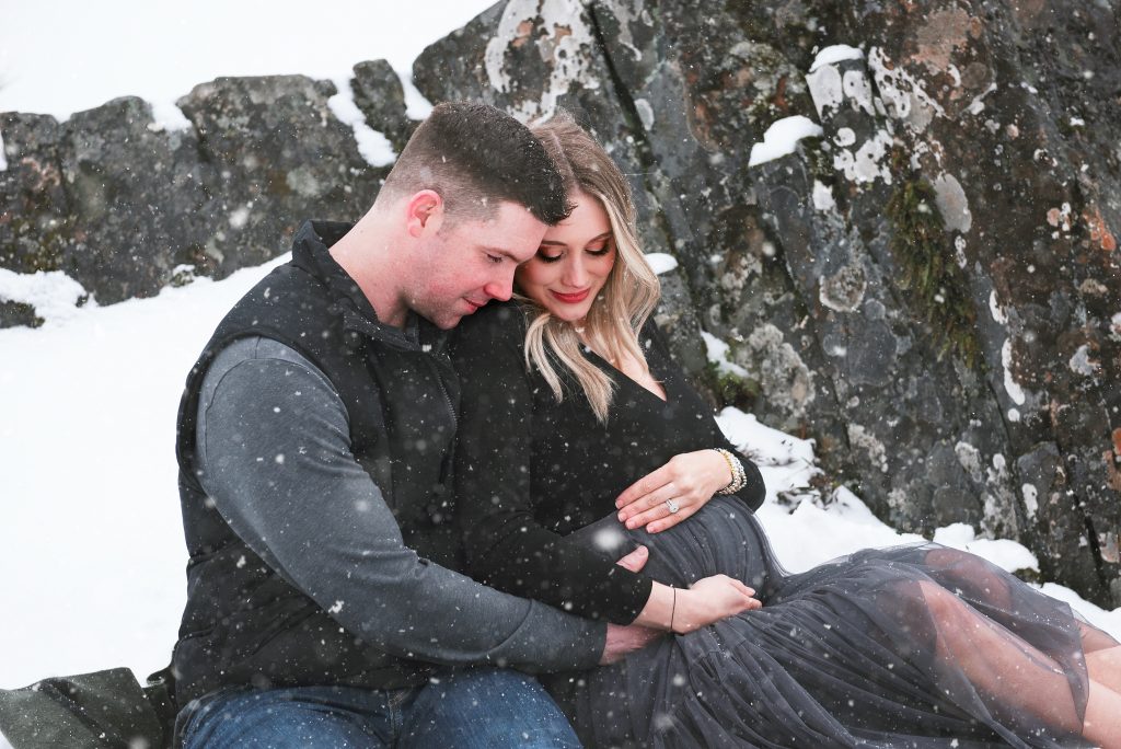 Pregnant couple cuddle in the snow on a mountain 