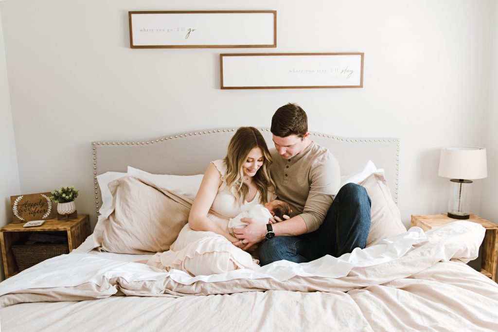 Parents wearing neutral colors on a bed snuggling their newborn daughter during an Ellensburg Family Photo Session