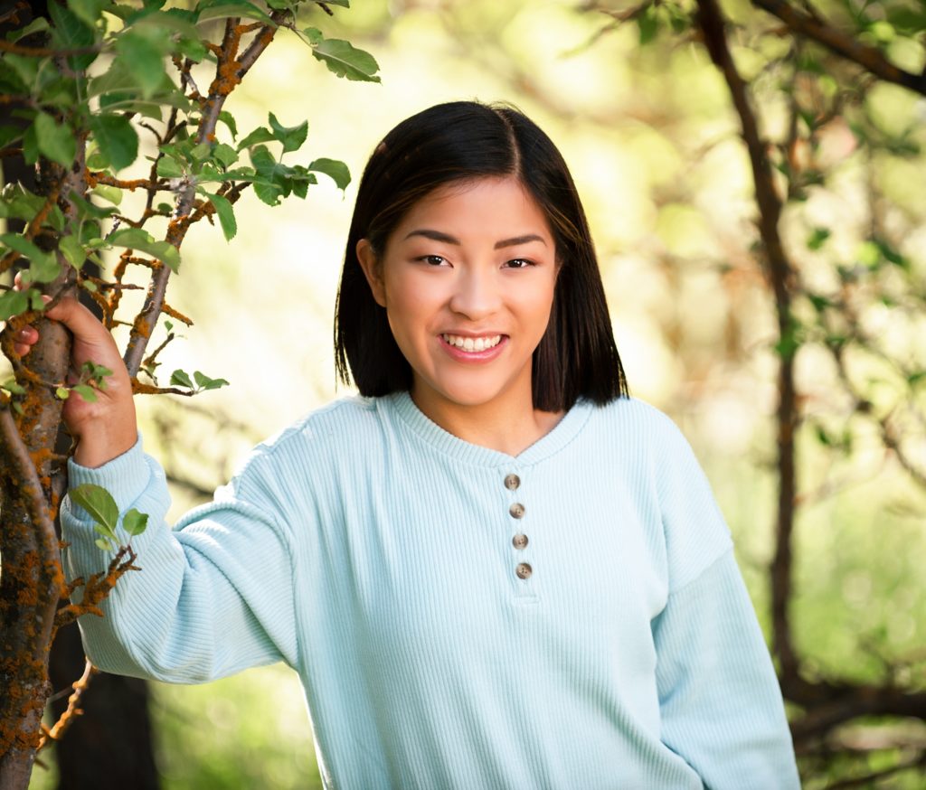 Asian girl with black hair smiles at camera wearing a mint colored sweater 
