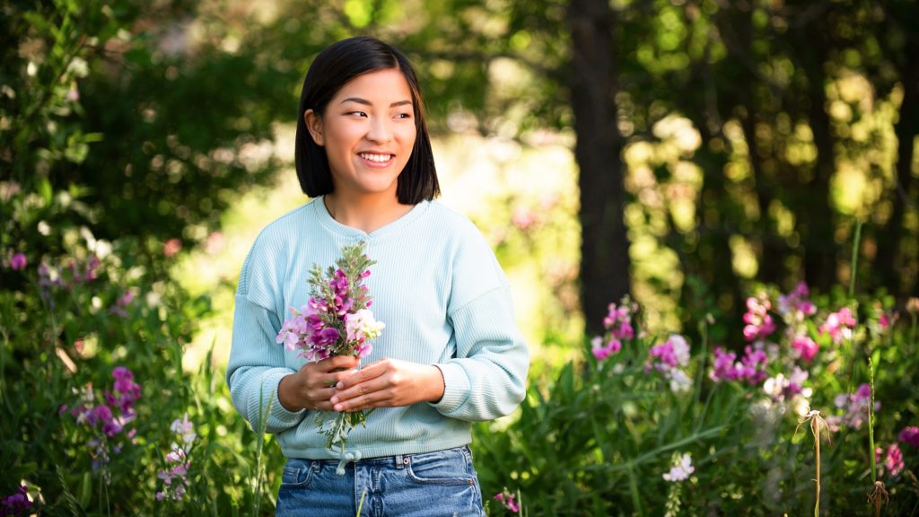 Pretty Asian Teenage Girl stands in a flower field and holds bouquet of wildflowers and smiles into the distance suncadia photographer