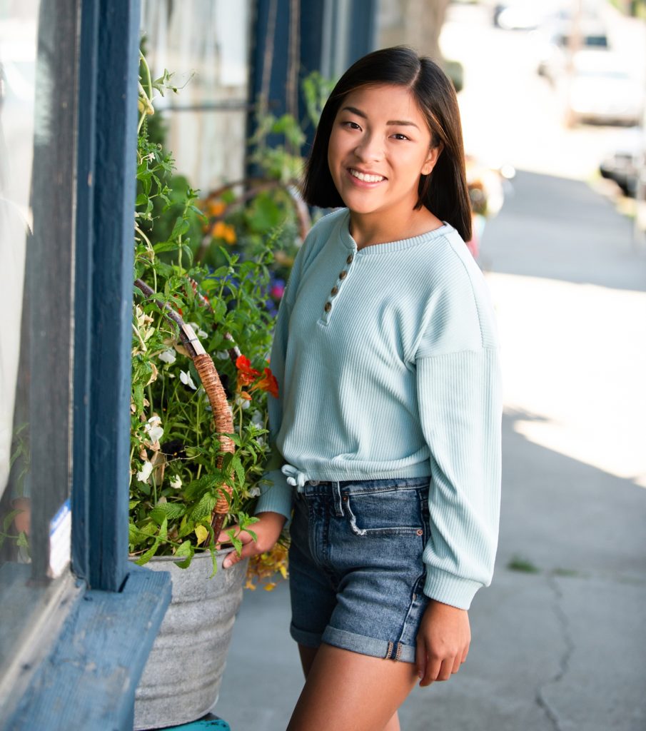 Pretty teenage girl poses near flowers on a shop lined street in Cle Elum WA