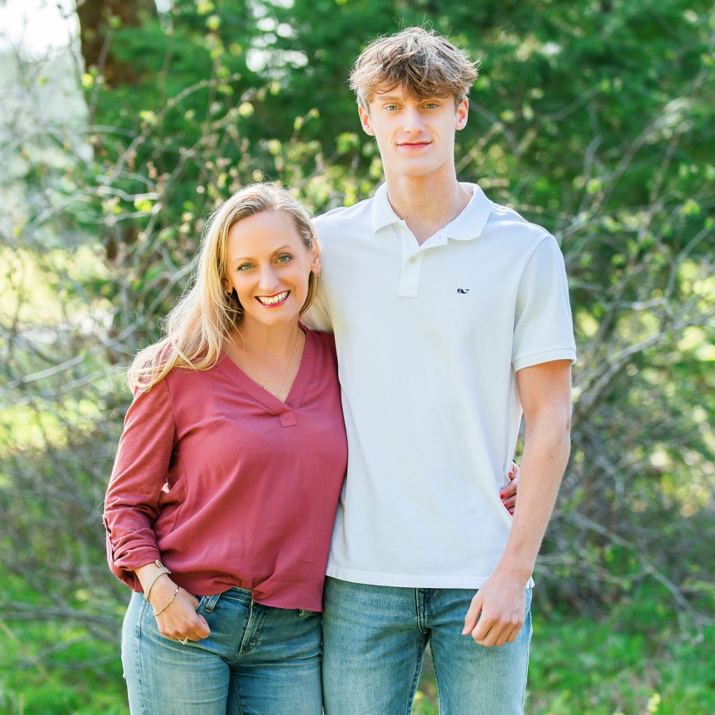 Mother and teenage son stand with arm wraped around eachother and smile 