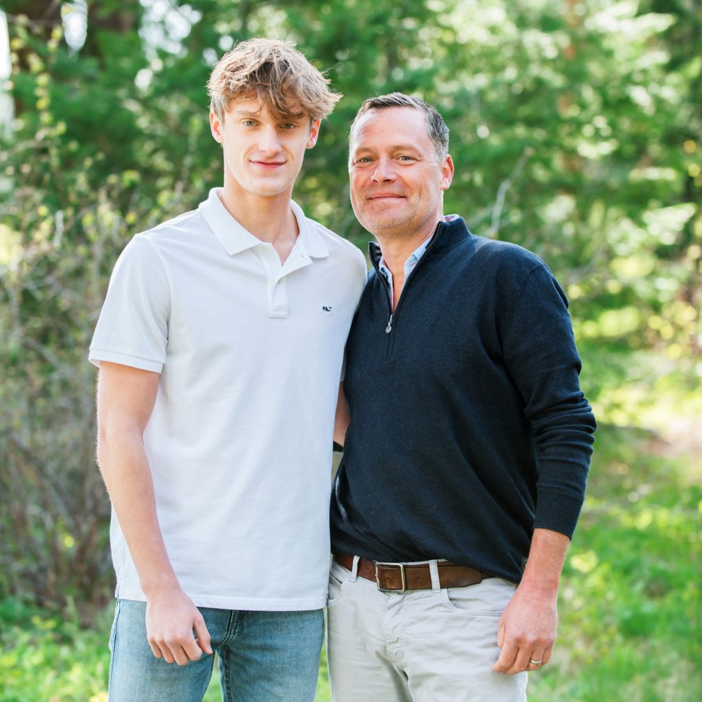 Dad poses with his arm wrapped around his teenage son 
