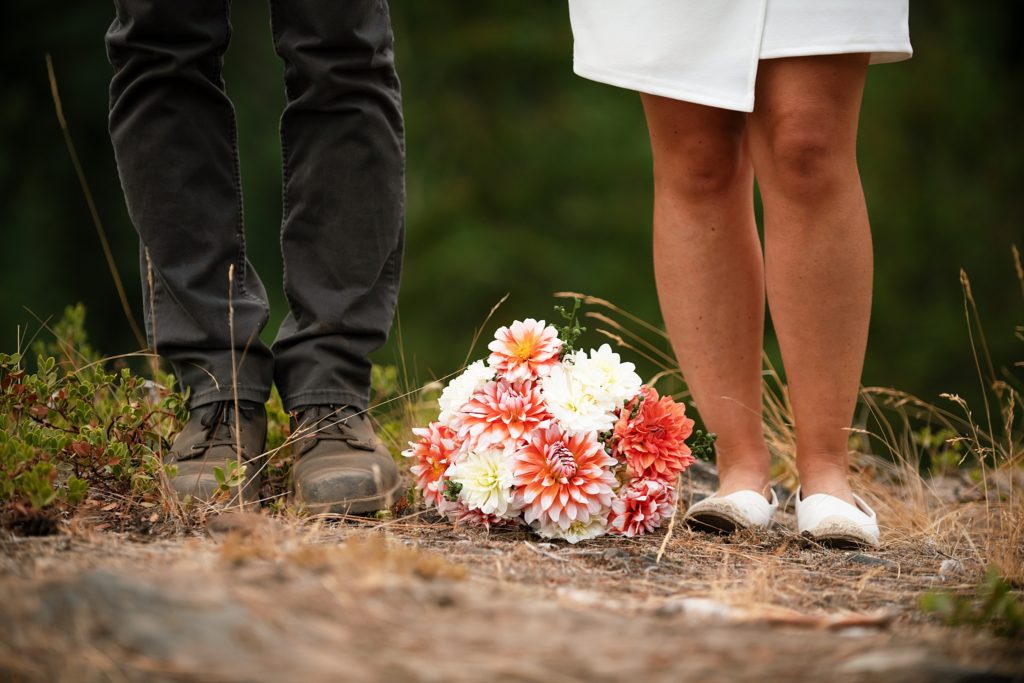 Photo of wedding bouquet laying between bride and grooms feet. 