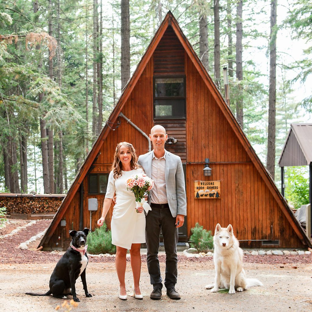 Bride and Groom stand in front of an A Frame cabin with their two dogs during an Elopement at Lake Cle Elum