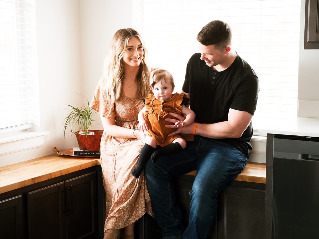 Mom, baby and dad sit on counter. Dad is smiling at baby.